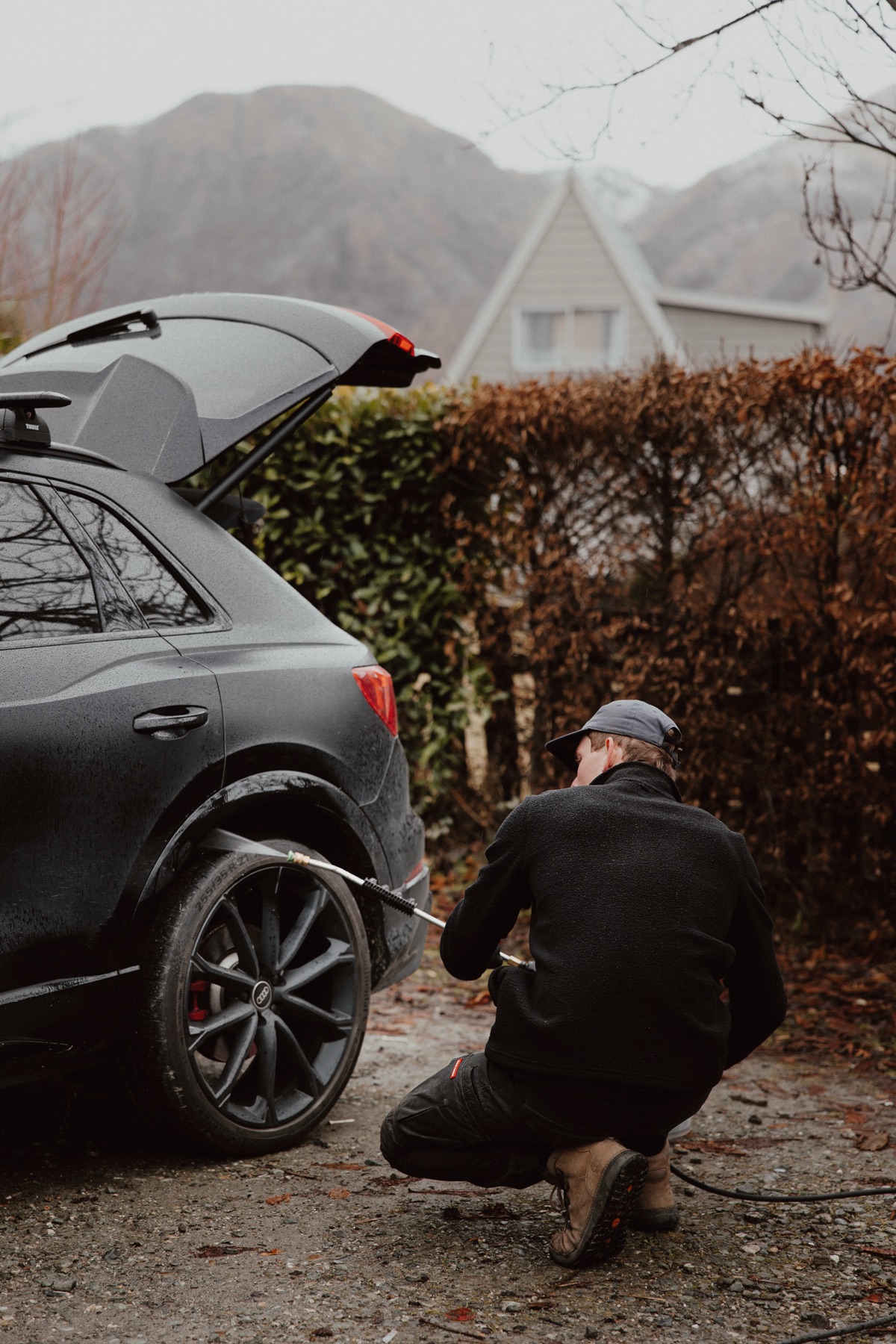 Mason crouched pressure washing rear wheel of black Audi in Queenstown