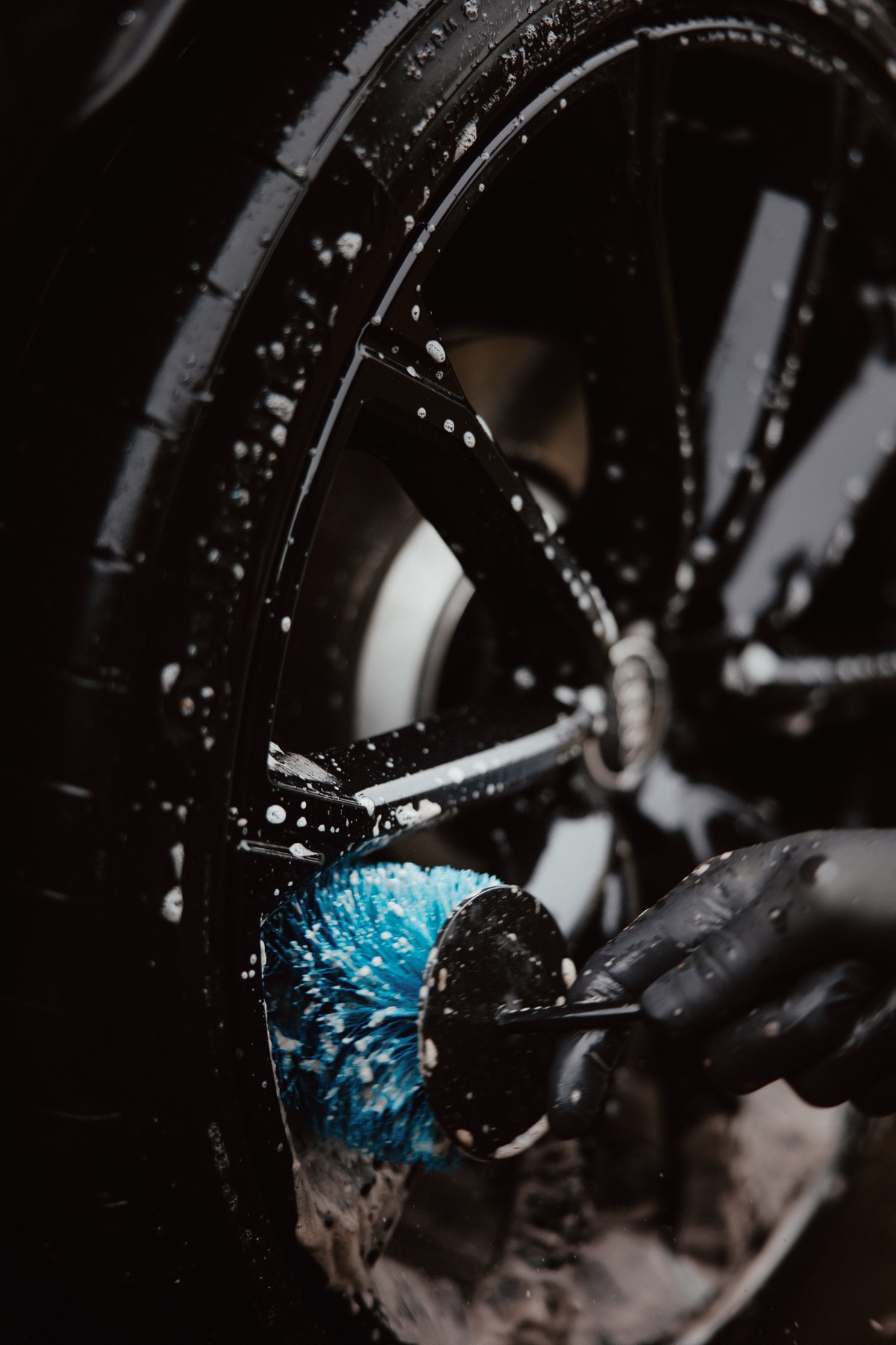 Close-up of blue detailing brush cleaning dark Audi wheel