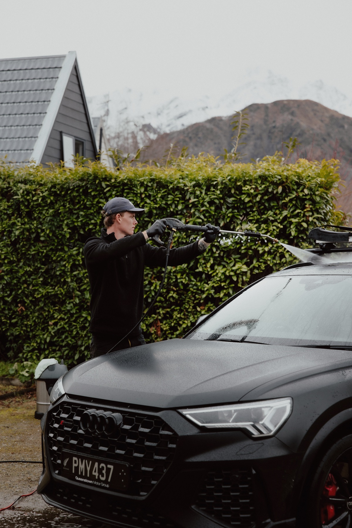 Mason pressure washing black Audi roof with snowy Queenstown peaks behind