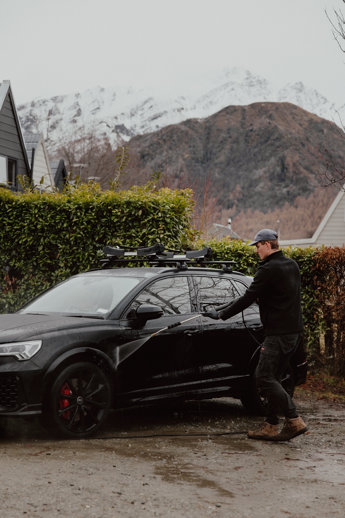 Mason pressure washing a black Audi RSQ3 with snow-capped mountains in the background - Queenstown