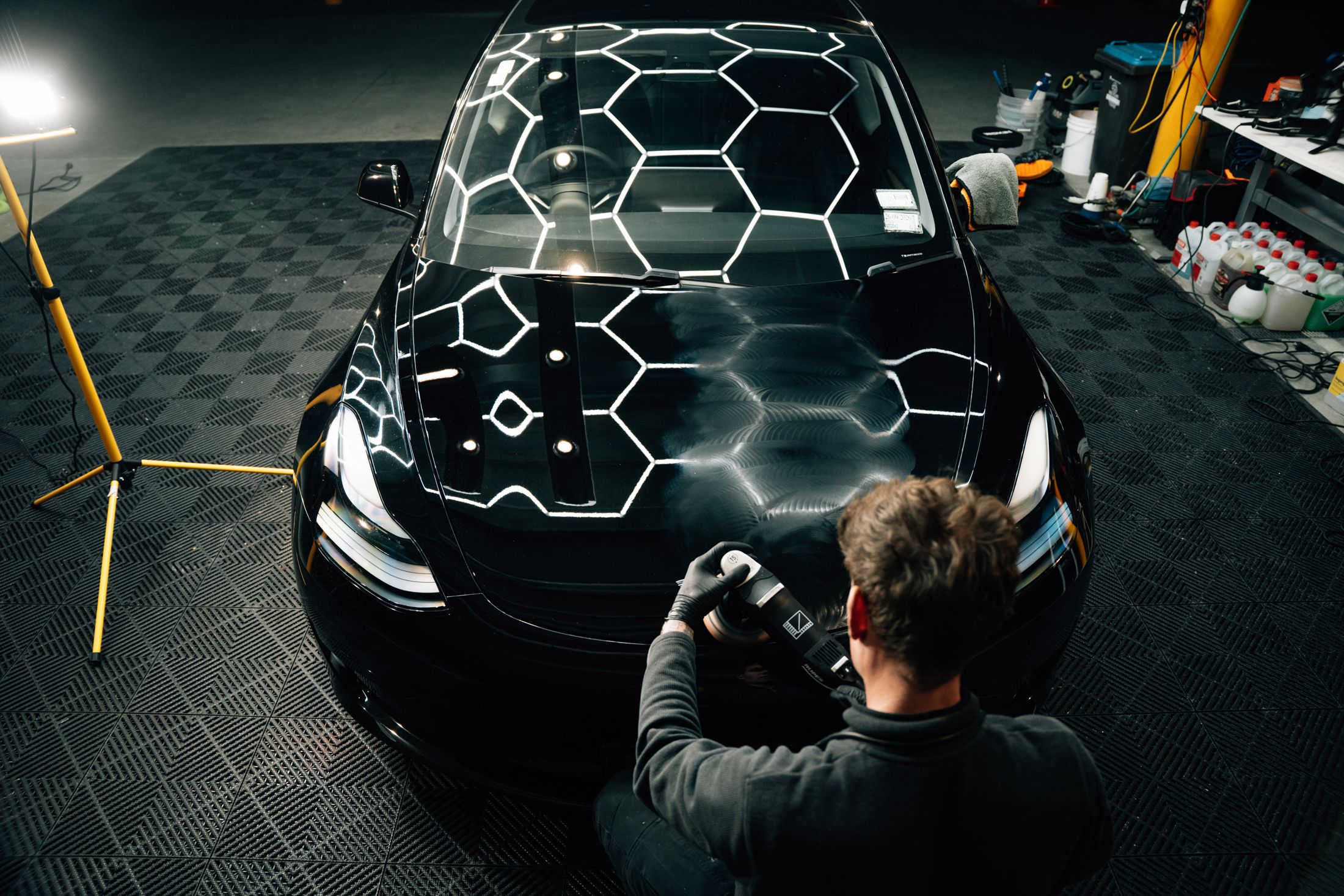 Machine polishing a black bonnet, half corrected, under the hex lights