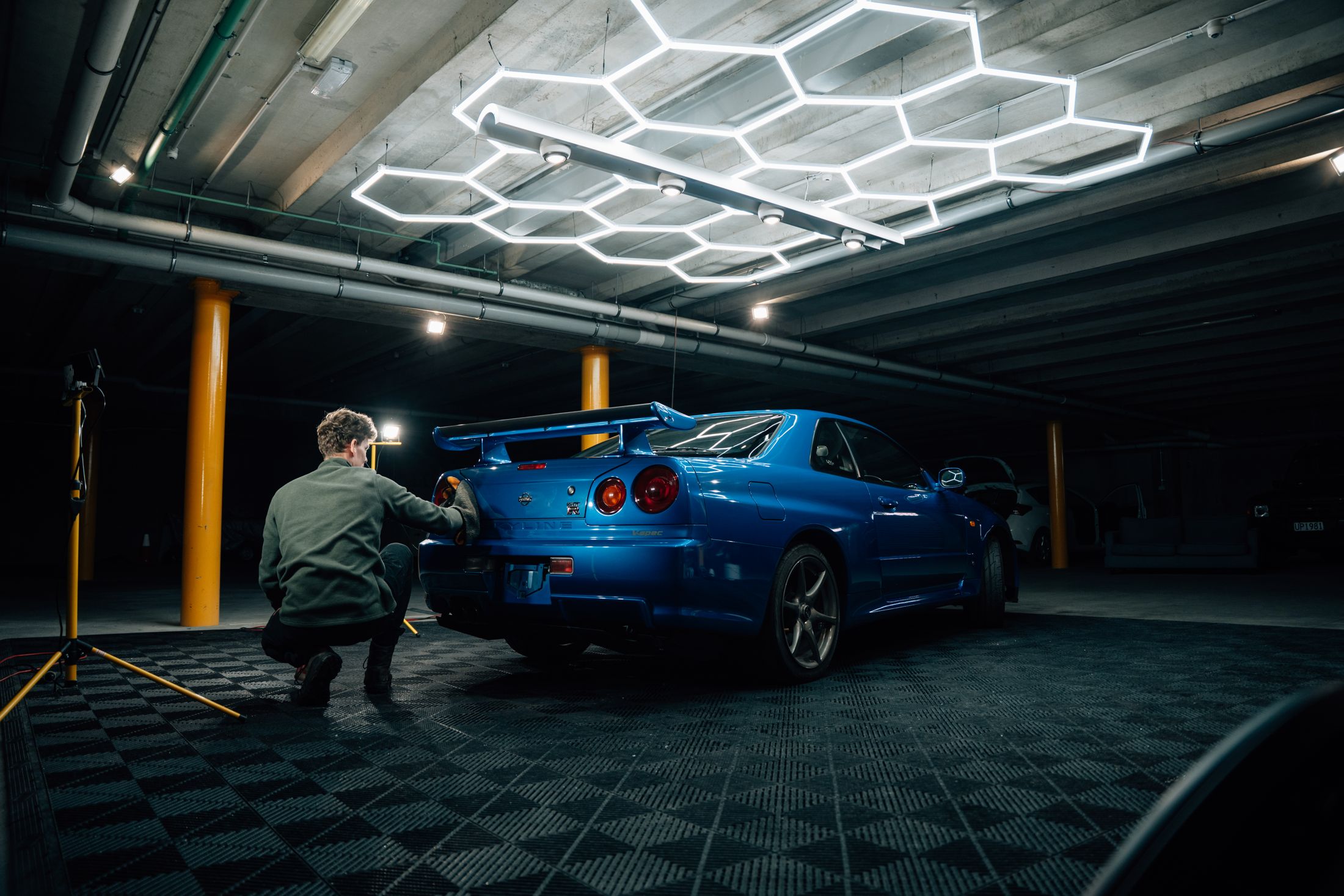 Mason working on a blue Nissan Skyline GT-R under the hex lights